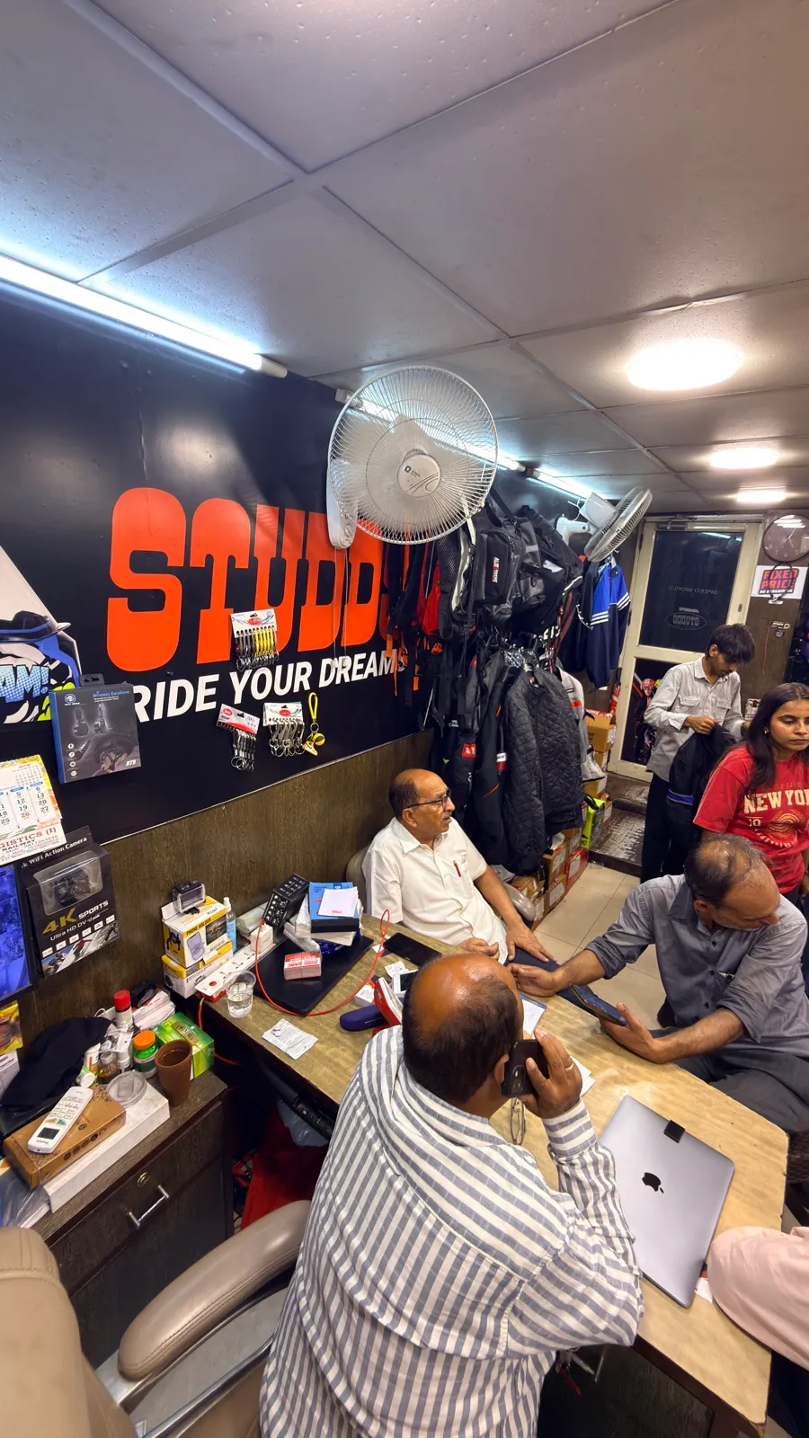 The owner of Speed World helping customers at the counter, under the Studds banner